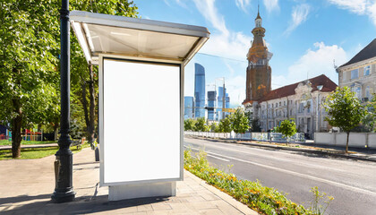 Vertical blank glowing billboard on the city street. In the background buildings and road with cars. Mock up. The poster on the street next to the roadway.