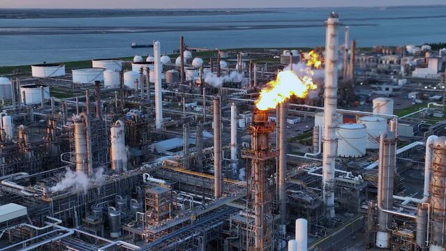 Aerial view of a chemical plant at sunset. Drone shot. Curling fire and cumin smoke filling the sky. Smoking chimneys from the factory. Chimneys of an oil refinery at sunrise pollute the environment