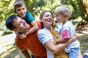 Fototapeta premium Family of four bonding in the park. Mother and father hugging with their sons.