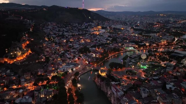 Tbilisi, Georgia. Scenic aerial view at twilight Of Famous Landmarks In Night Illuminations. Cityscape. Overview of the Kura (Mtkvari) River in Old Town, Tbilisi city central park and Bridge of Peace