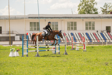 A young girl goes in for horse riding. A horse jumps over a barrier.