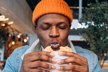 African American man savoring delicious burger in cozy cafe, capturing the joy of eating. Hungry...