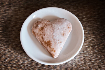 Honey gingerbread in the shape of a heart lies on a white plate on a dark table. View from above