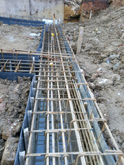 Construction site with rebar placement for foundation footing, steel reinforcement, and rebar grid. Preparation for concrete pouring. Urban residential development.