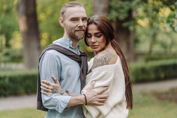 Fototapeta premium Love, hug and happy with couple in park for romance, bonding and summer vacation. Loving young couple hugging and smiling together on nature background. Beautiful girl with tattooed body outdoor.
