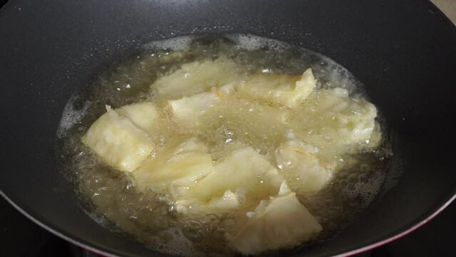 Woman's hand frying cassava or singkong traditional Indonesian snack in a pan, shot with handheld movement.