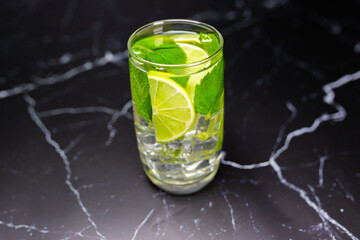 Mojito cocktail with lime, mint and ice on the black marble, dark background. Sparkling refreshing water. Space for text.  