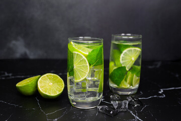 Mojito cocktail with lime, mint and ice on the black marble, dark background. Sparkling refreshing water. Space for text.  