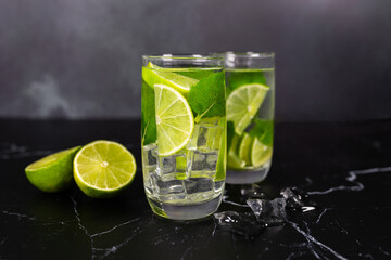 Mojito cocktail with lime, mint and ice on the black marble, dark background. Sparkling refreshing water. Space for text.  