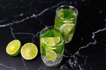 Mojito cocktail with lime, mint and ice on the black marble, dark background. Sparkling refreshing water. Space for text.  