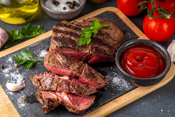 Grilled beef steak on wooden cutting board with ketchup sauce and condiments, top view copy space
