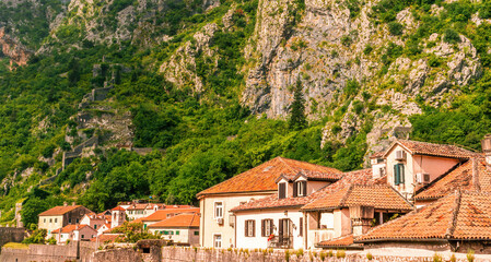 Fototapeta premium landscape of beautiful vintage houses with orange tile roofs in vintage venetian style to amazing high green mountain with ancient buildings on slopes and nice cloudy sky on background