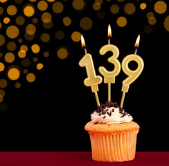 Birthday candle with cupcake - Number 139 on black background with out of focus lights