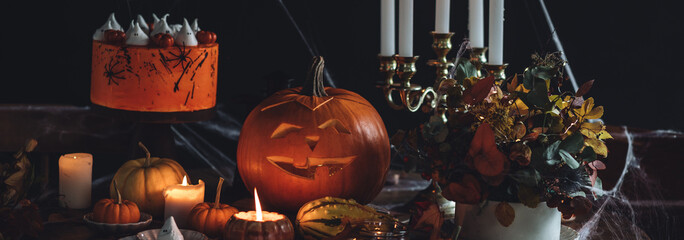 Beautiful table with homemade delicious cake for Halloween party with meringue ghosts and chocolate pumpkins. Candles in chandelier, spider web, jack-o-lantern for festive holiday decoration. Banner