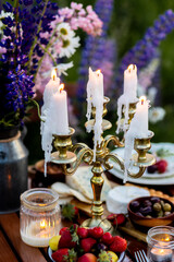 Beautiful elegant outdoor arrangement in meadow with purple blue lupins. Perfect date, private wedding or romantic marriage proposal. Summer, sunset, golden hour. Appetisers, rose wine, strawberry