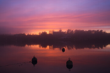 The quiet evening landscape captures the tranquil beauty of the small coastal fjord town. Black buoys in the foreground