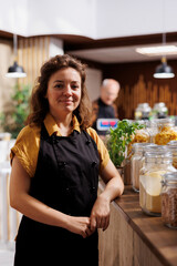 Portrait of smiling zero waste shop storekeeper next to ethically sourced low carbon footprint bulk products. Joyful woman working in green living local neighborhood store using renewable energy