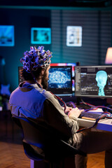 Man with EEG headset on writing code allowing him to transfer mind into computer virtual world,...