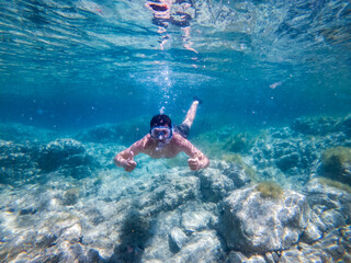 Man diving underwater in clear cristaline water pointing his thumbs up