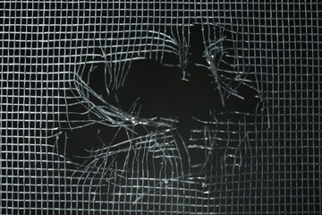 Torn window screen against black background, closeup