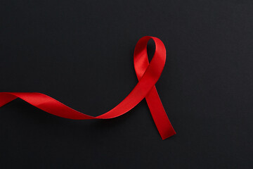 Red awareness ribbon on black background, top view