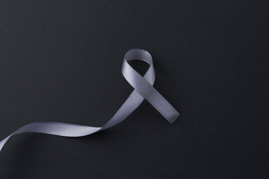 Grey awareness ribbon on black background, top view