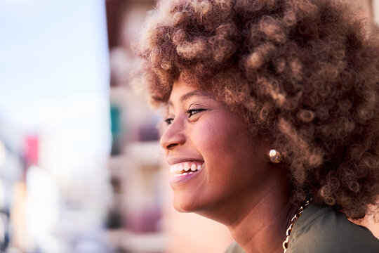 Side view of a cheerful African young woman outdoors enjoying the view. Close-up of a black woman in profile smiling. Copy space image.