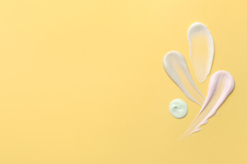 Samples of face cream on yellow background, top view. Space for text