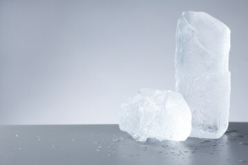 Pieces of clear ice and water drops on light grey table. Space for text