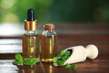 Bottles of mint essential oil and fresh leaves on wooden table