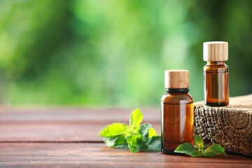 Bottles of mint essential oil and fresh leaves on wooden table, space for text