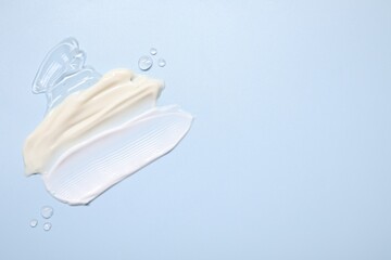 Face cream and gel on light blue background, top view. Space for text