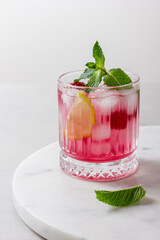 Raspberry gin and tonic with ice in a glass on a light background