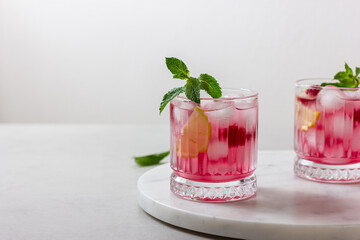 Cold raspberry drinks with ice in a glass on a light background