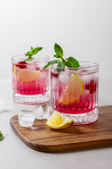 Raspberry gin and tonic with ice in a glass on a light background