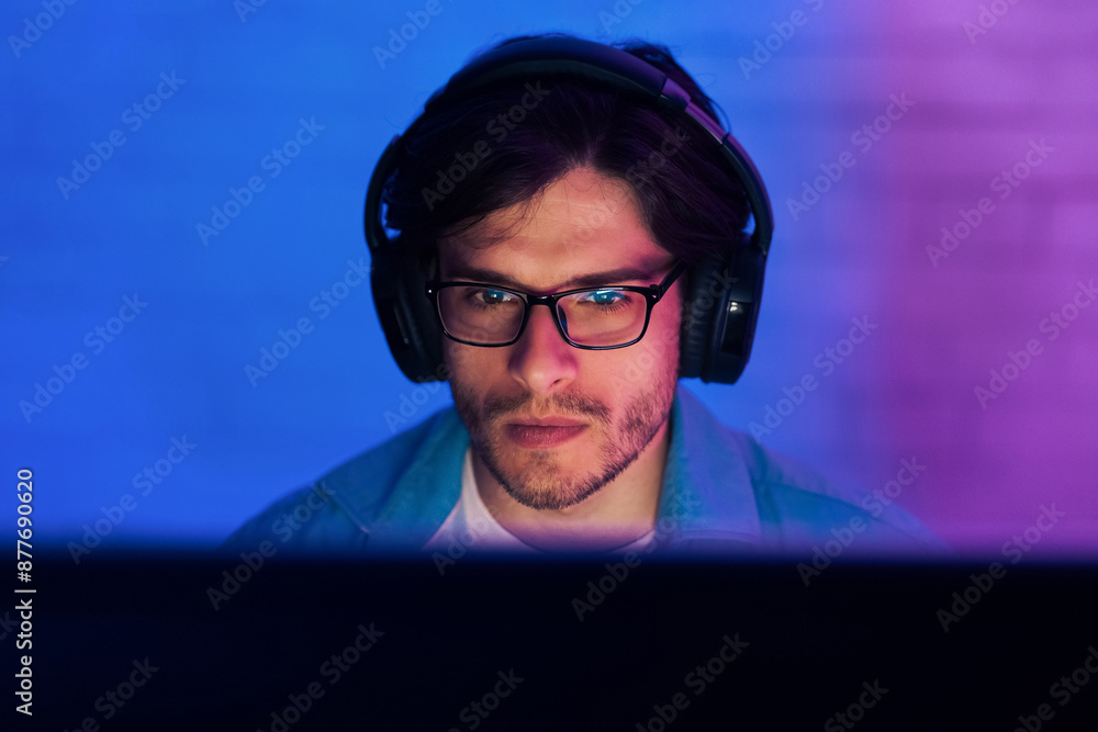 Poster a man in glasses and headphones sits in front of a computer screen, his face illuminated by blue and