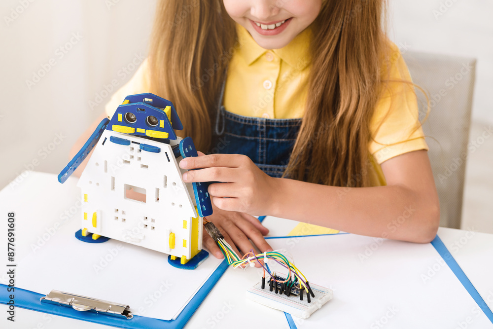 Poster a young girl is sitting at a table, constructing a robot out of colorful plastic pieces. she is hold