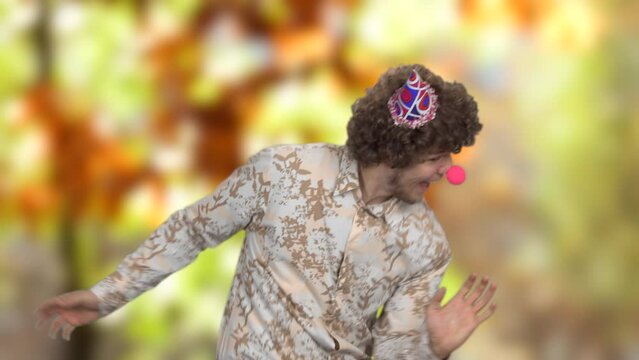 Portrait of a young male clown dancing hard outdoors. Blurred autumn park in the background.