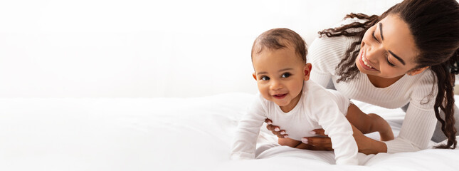 Black Mom Posing With Baby Toddler Holding Helping Her Son Crawl On White Studio Background. Happy Young Mother Caring For Child Infant Bonding And Playing With Cute Little Boy. Panorama, Copy Space