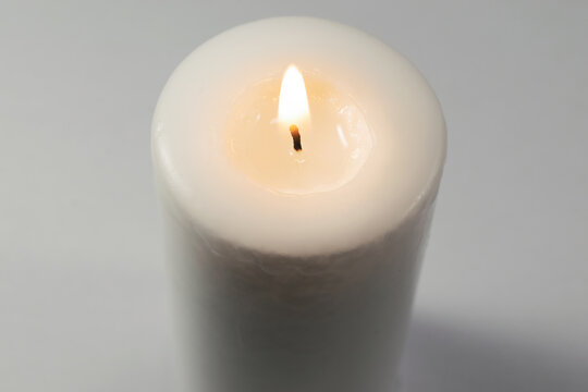A lighted white candle burning isolated on white background with low light shadow