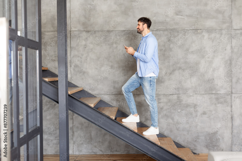 Poster this image shows a man walking up a modern staircase in a home. the man is casually dressed in a blu