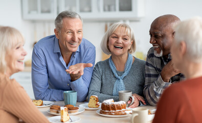 Multiracial group of happy senior people sitting around table drinking tea with cake and having...