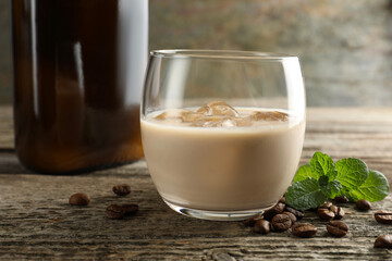Coffee cream liqueur in glass, mint and beans on wooden table, closeup