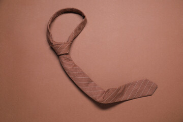 One striped necktie on brown background, top view