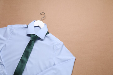 Hanger with shirt and necktie on beige background, top view. Space for text