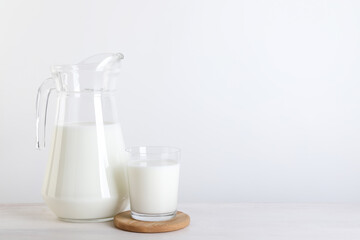 Jug and glass of fresh milk on wooden table, space for text