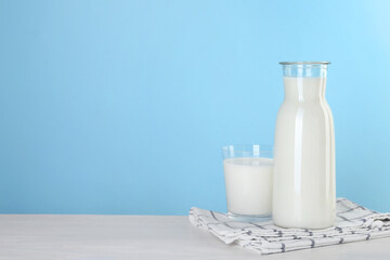 Carafe and glass of fresh milk on table against light blue background, space for text