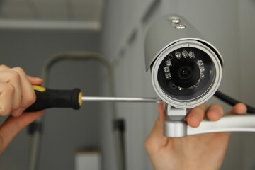 Technician with screwdriver installing CCTV camera on wall indoors, closeup