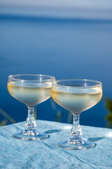 Cold sparkling wine, cava or champagne in two coupe glasses on table with blue sea water view