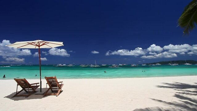 Sun umbrellas and beach chairs on tropical beach with palm trees. Summer vacation. Boracay